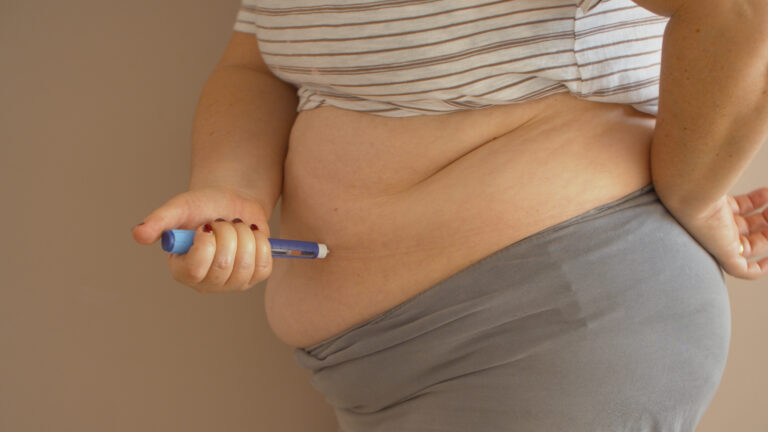 Obese woman stuck needle from syringe into her exposed side of the body giving herself shoot of insulin.